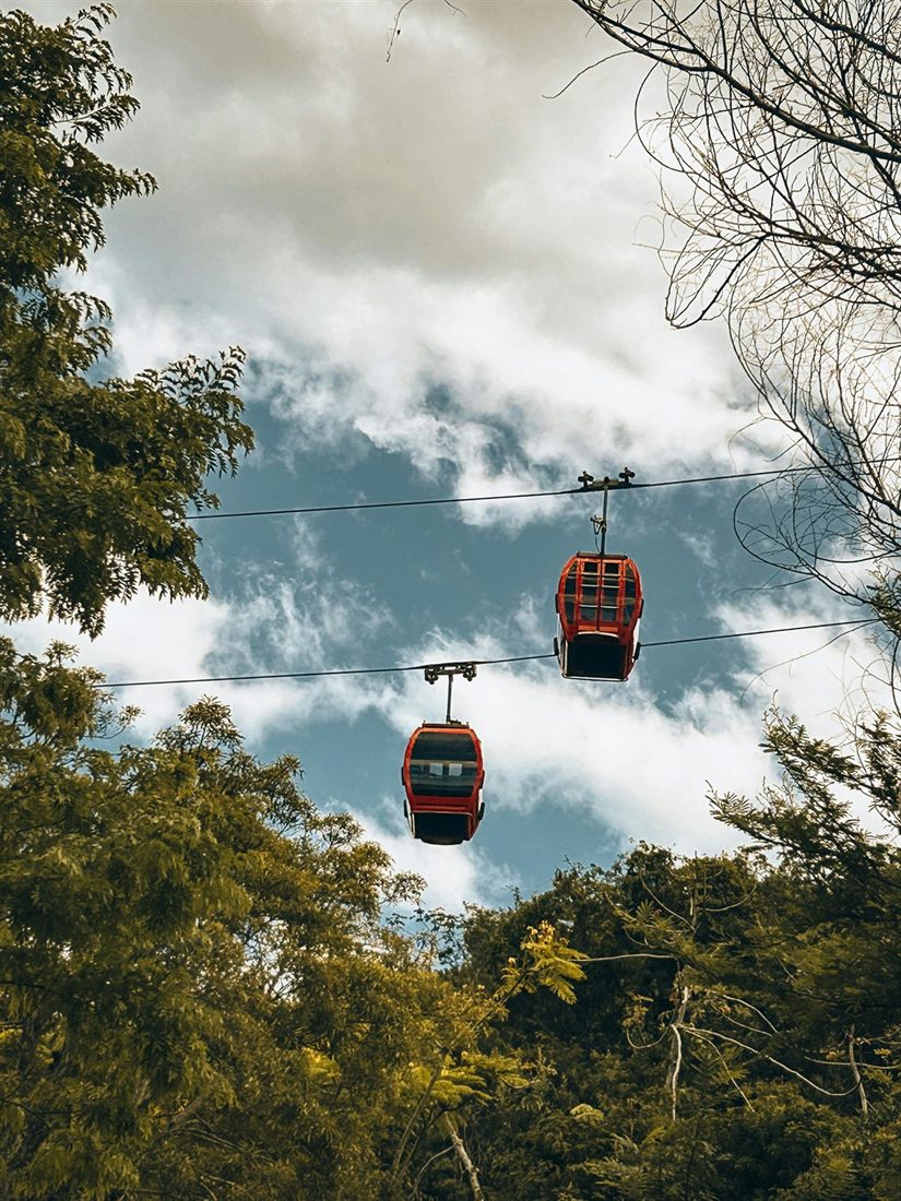 Two red cable-car cabins of the Unipraias park against a cloudy sky, with trees on both sides
