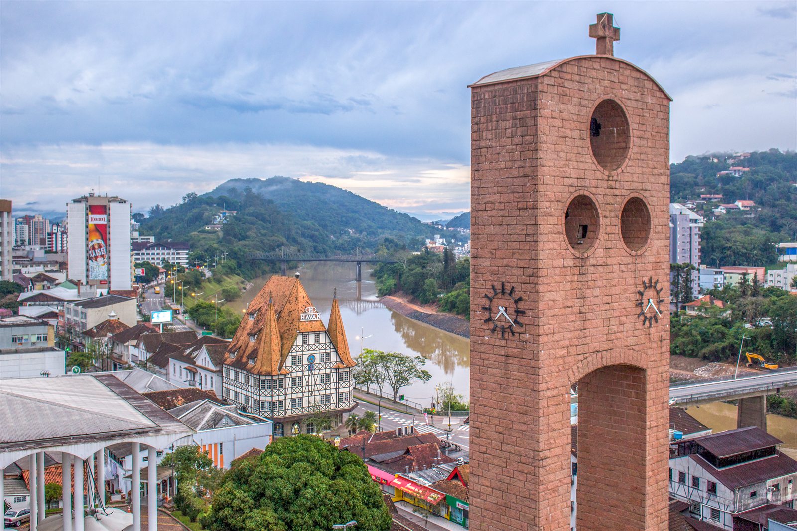 The center of Blumenau seen from above: the cathedral's brick bell tower, the half-timbered Castelinho, the Itajaí-Açu river and the Ponte de Ferro
