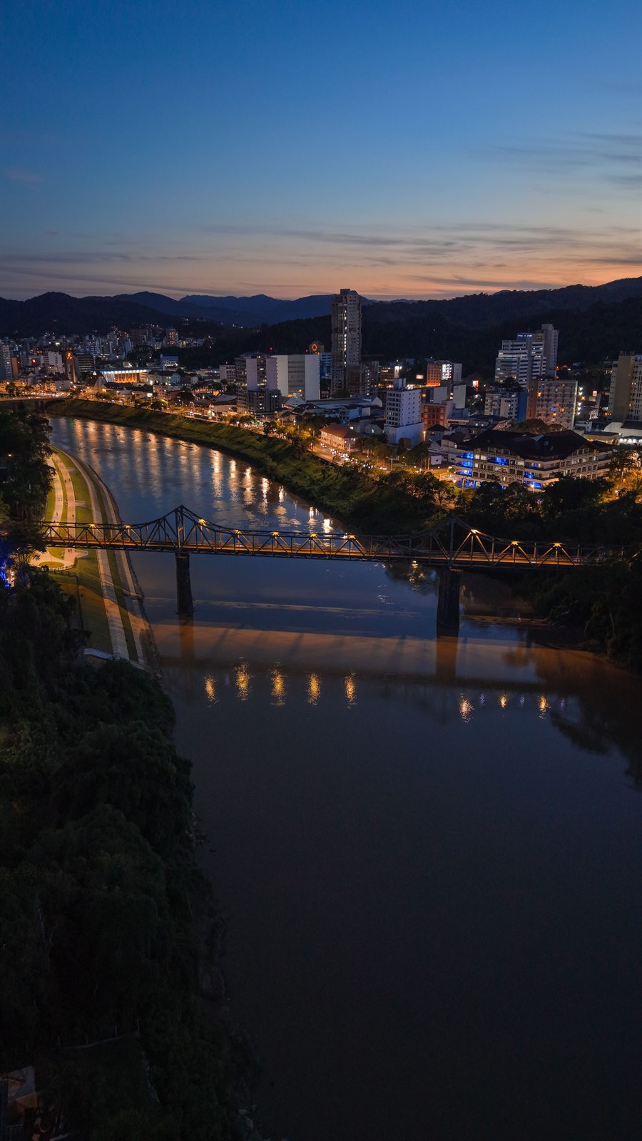 Blumenau at twilight seen from above: the Itajaí-Açu river, the Ponte de Ferro and the lit city center