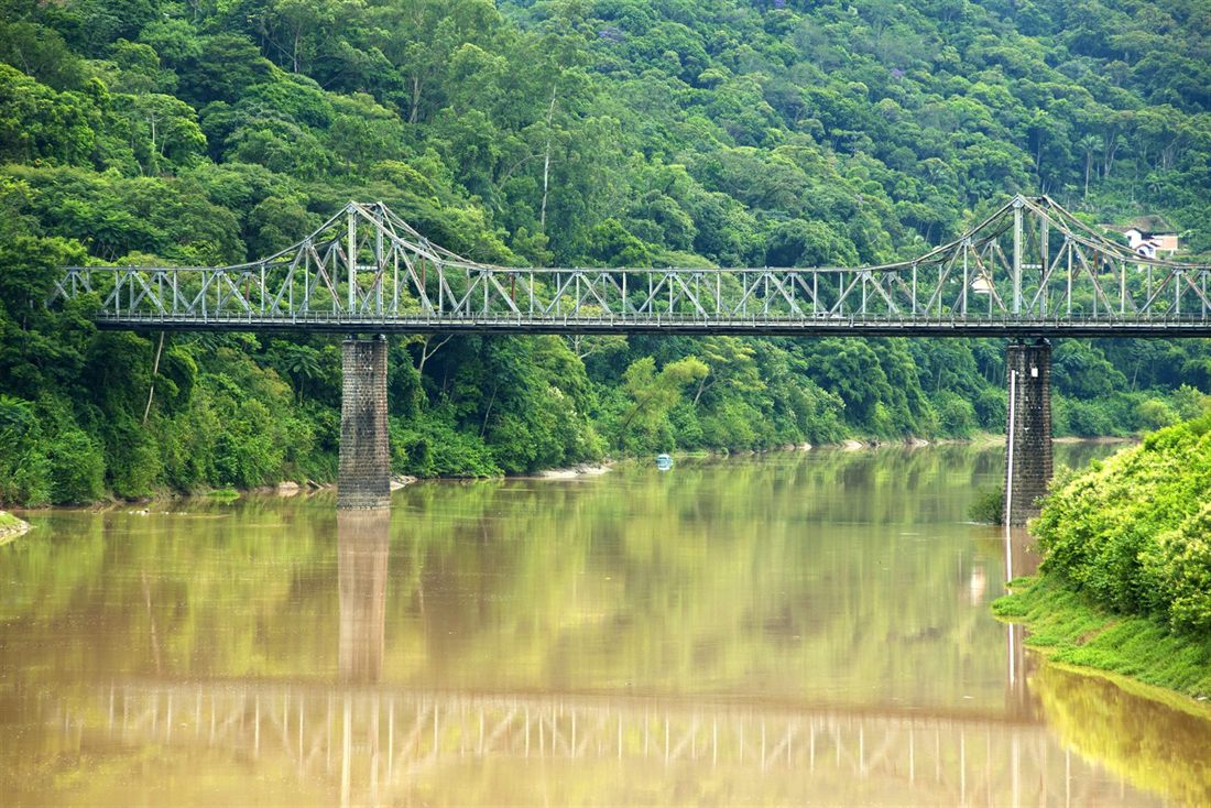 The Ponte de Ferro, an iron bridge over the Itajaí-Açu river, with forested hills behind