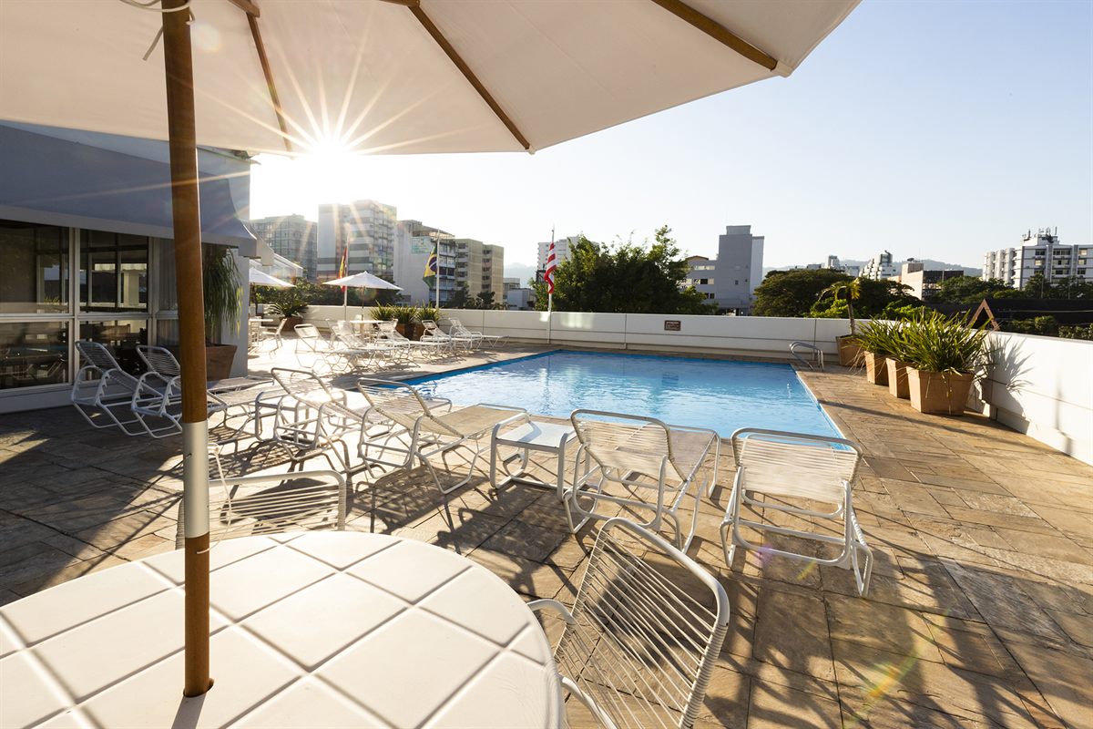 The rooftop pool of the Plaza Blumenau Hotel at the end of the day, white loungers and the city center behind