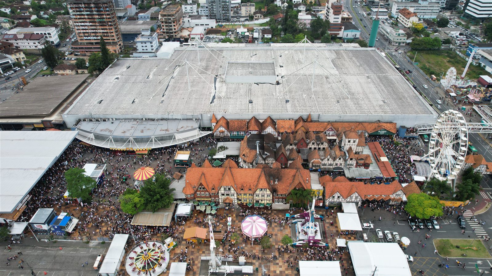 The Parque Vila Germânica from above during the Oktoberfest: the pavilion roof, the half-timbered houses, the Ferris wheel and the crowd filling the square