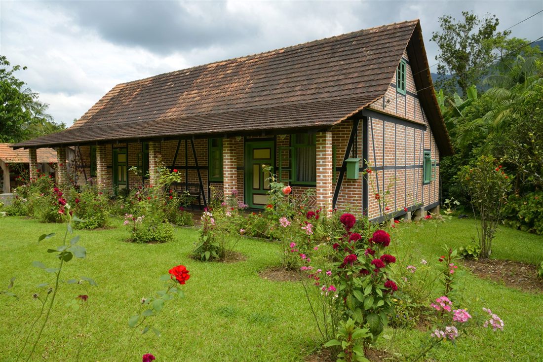 A half-timbered brick farmhouse with green shutters and a flower garden on the Rota do Enxaimel, Pomerode
